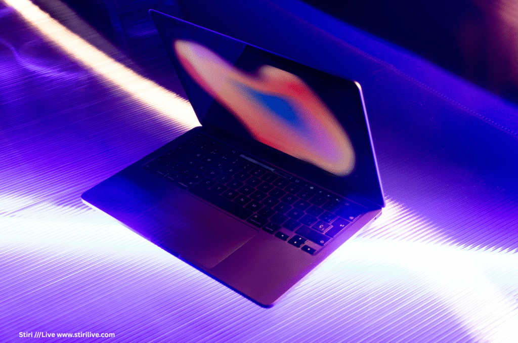 Laptop deschis cu ecranul emițând o aura luminoasă în tonuri de albastru și roz, pozat pe o suprafață reflectantă, ilustrând potențialul dispozitivelor de calcul în aplicarea tehnologiilor inovatoare din 2025, precum AI etică și biotehnologie, pentru o lume mai conectată și eficientă.